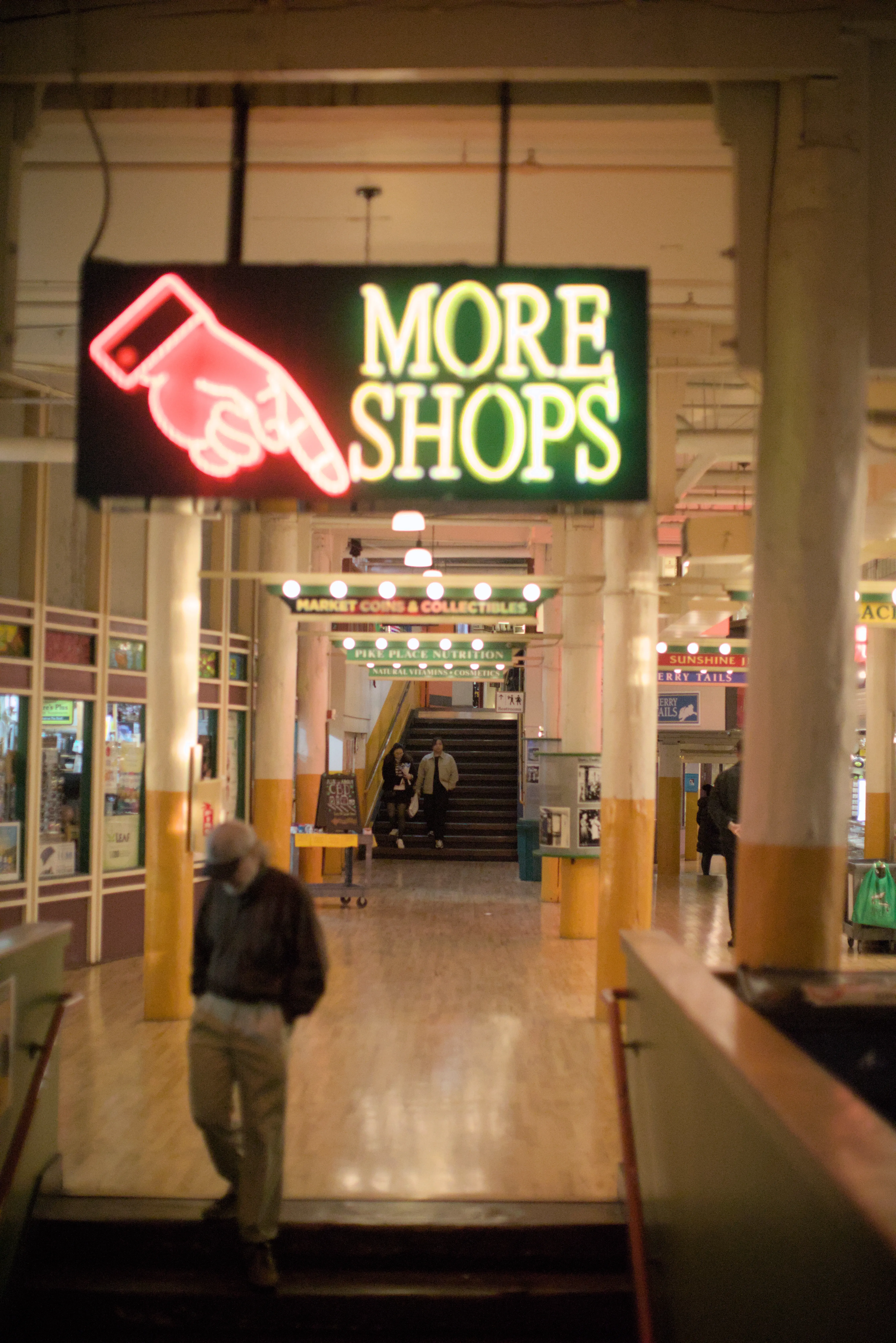 A man walks down the stairs away from a sign advertising More Shops at Pike Place Market