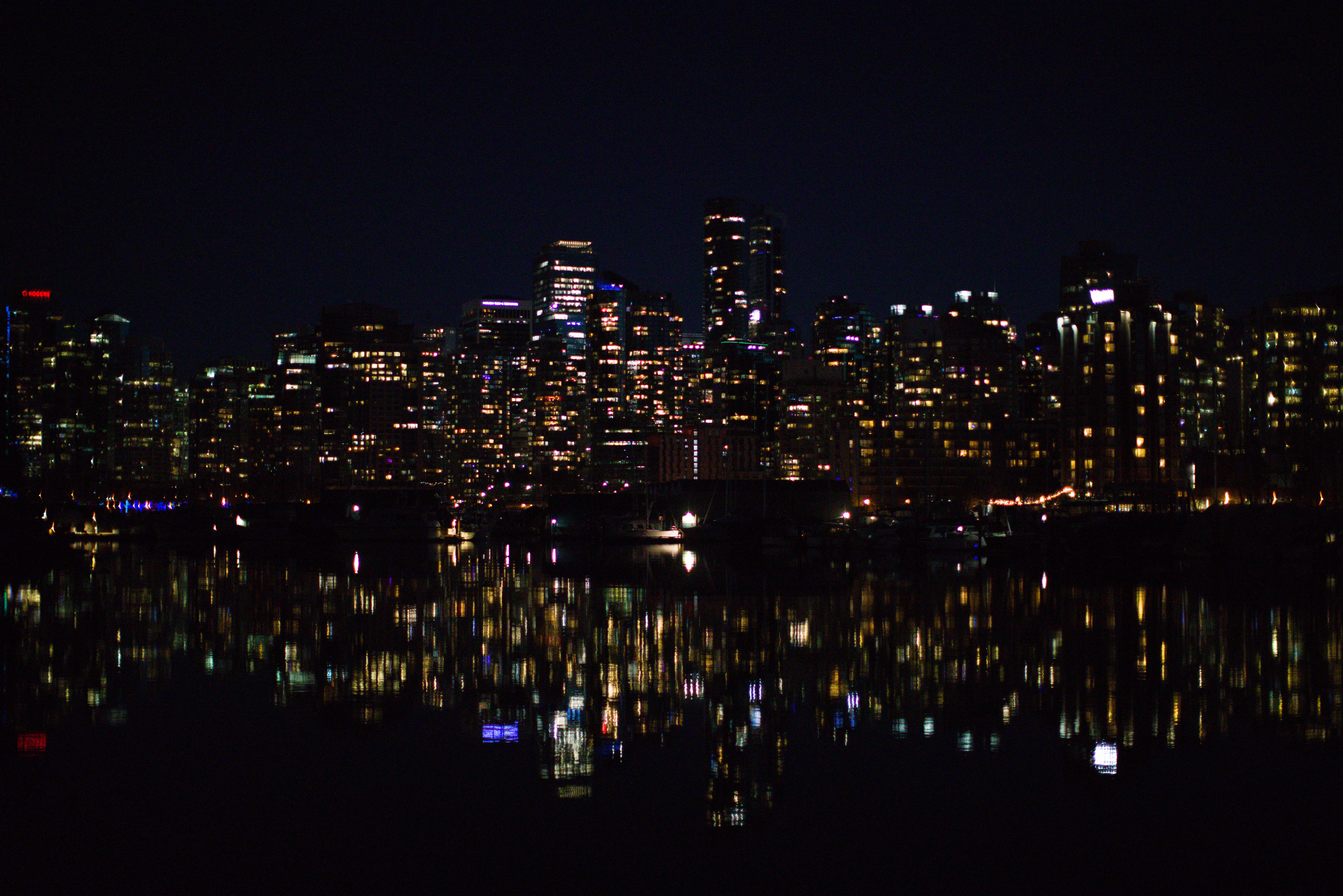 The lit up skyline of Vancuver reflects in the water between it and Stanley Park