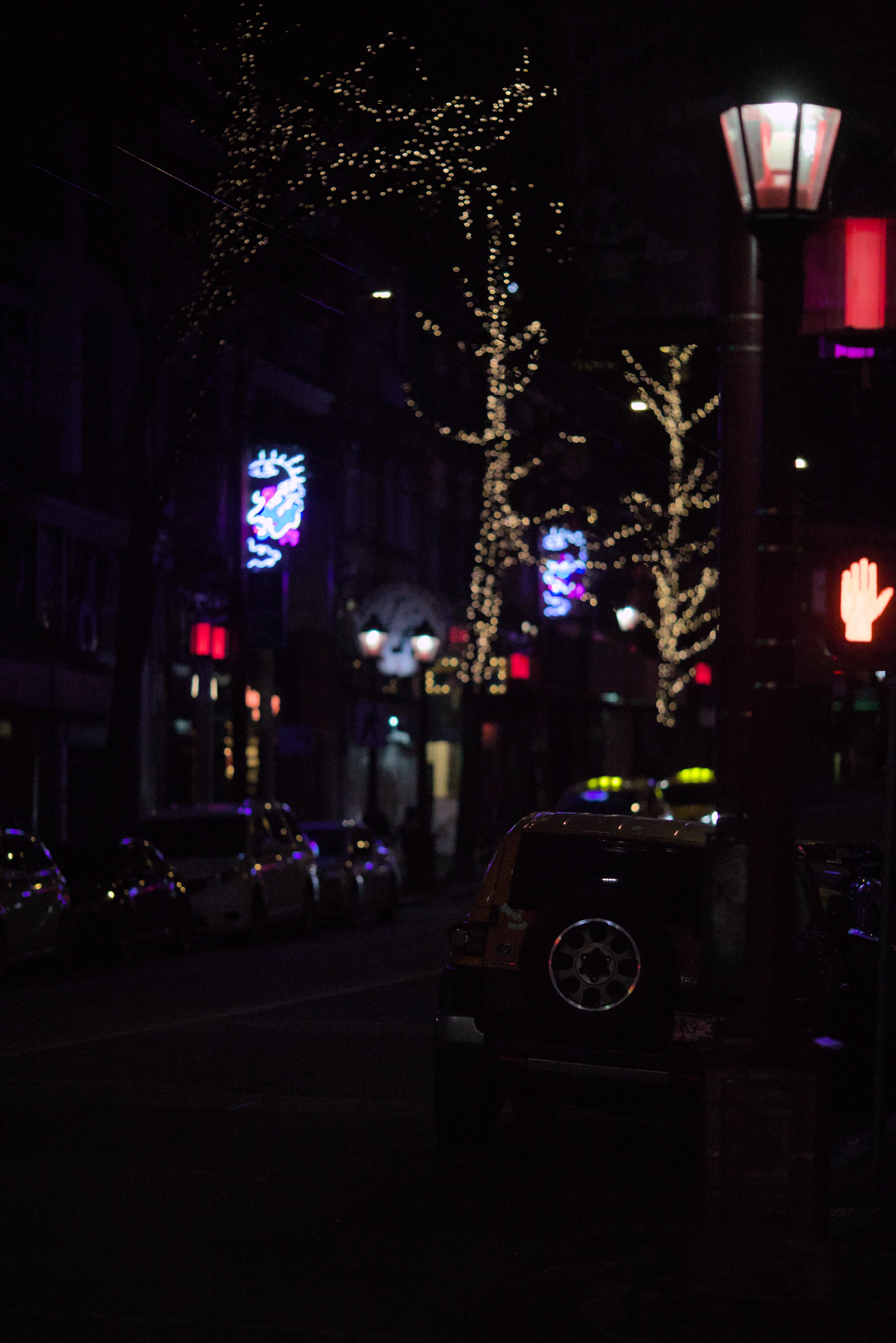 A vancuver street full of cars with neon dragon signs and christmas lights