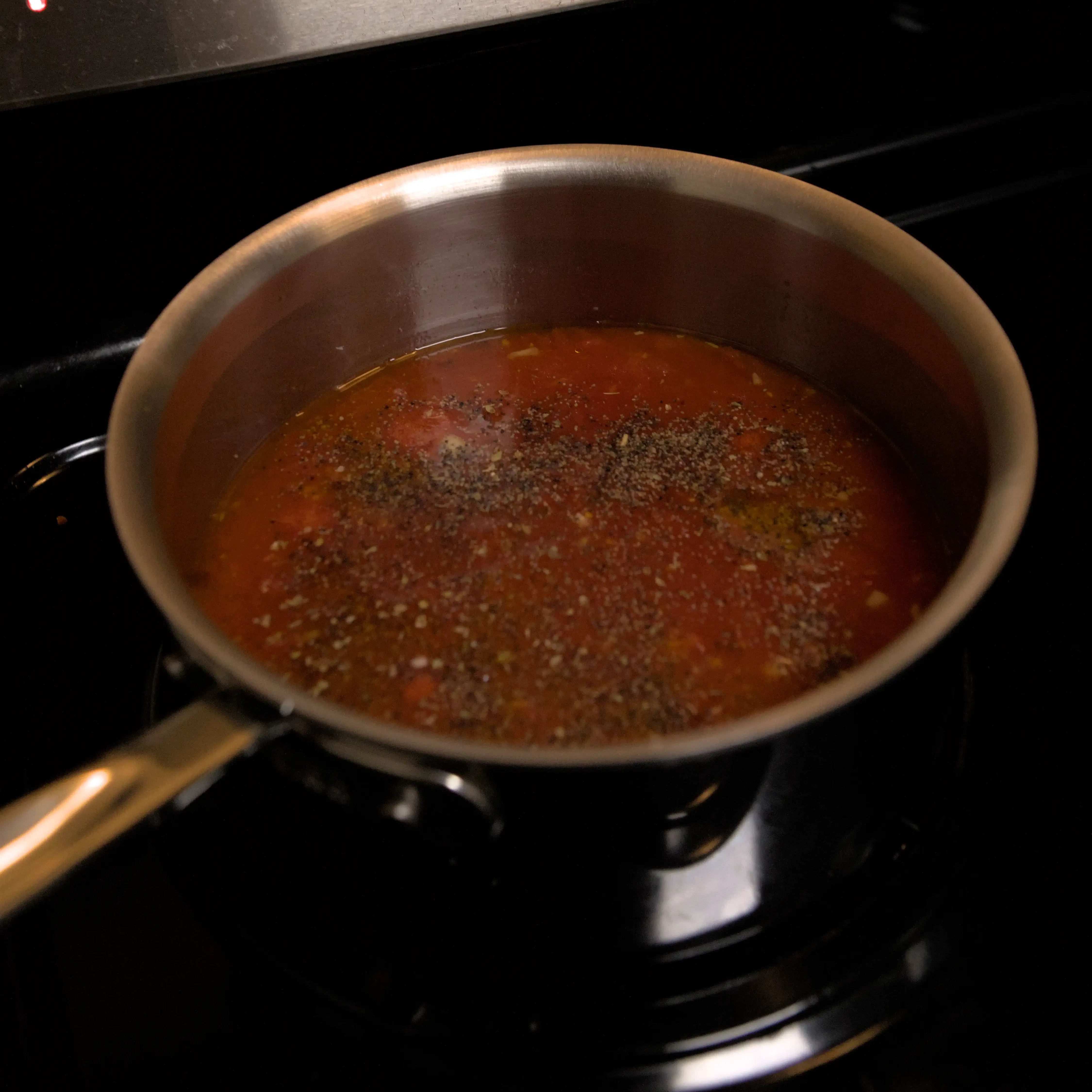 Sauce pan with spices layered on top of tomato sauce